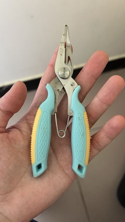 Fishing pliers held in a hand, photographed on a phone under office lighting