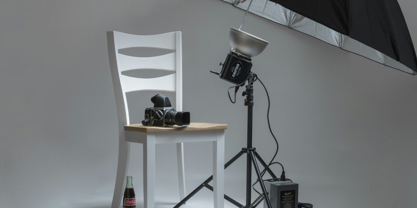 A product photography studio: strobe head, silver umbrella, medium-format camera and a bottle on a seamless backdrop